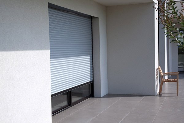 Volet roulant traditionnel gris devant une baie donnant sur une terrasse