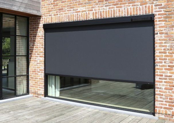 Store Screen ZIP gris partiellement abaissé devant une baie sur une façade en briques